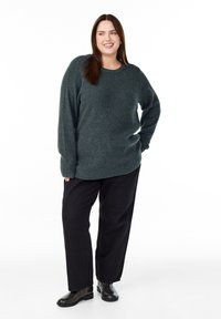 Megzta tamsiai žalia palaidinė su laisvu siluetu ir ilgomis rankovėmis, derinama su juodomis plačiomis kelnėmis ir juodais auliniais batais.