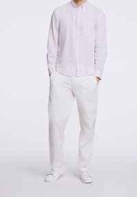 Camicia a maniche lunghe con bottoni, leggermente a righe, in rosa pallido e bianco, abbinata a pantaloni larghi in lino bianco e sneakers bianche.