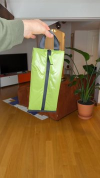 Saco retangular verde e brilhante com fecho de correr e acentos pretos, apresentando duas alças curtas cinzentas para transporte.