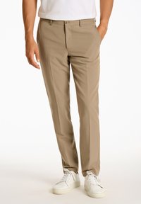 Beige Hosen aus glattem Stoff, mit klassischer Passform, vorderen Taschen und Knopfverschluss. Kombiniert mit weißen Sneakers.