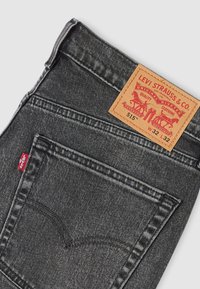 Μαύροι τζιν από τζιν υλικό με ξεβαμμένο φινίρισμα, που διαθέτουν δερμάτινο ταμπελάκι με την επιγραφή "Levi Strauss & Co." και μια κόκκινη ετικέτα στην αριστερή πίσω τσέπη.