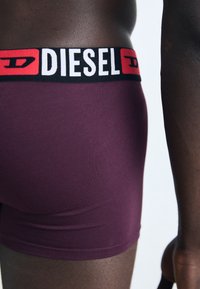 Boxers en bordeaux avec une ceinture logos "DIESEL" noire et rouge. Texture lisse avec un design ajusté et une longueur mi-cuisse.