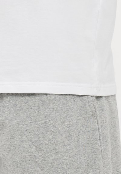 Weißes Baumwoll-T-Shirt am Saum kombiniert mit grauen Baumwoll-Sweatpants. Das T-Shirt hat ein schlichtes Design; die Sweatpants bestehen aus einem weichen, strukturierten Stoff.