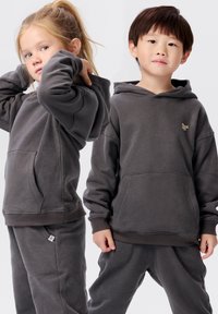 Grijze hoodies met kangaroo zakken en geribbelde manchetten, gecombineerd met bijpassende joggingbroeken. Zachte textuur, minimalistisch ontwerp, gouden logodetail.