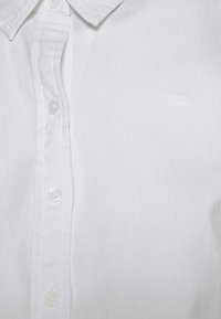 Vit knapp-up skjorta i bomull, med krage, fem knappar fram och en subtil pr präglad logotyp på bröstet.