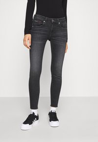 Vaqueros negros ajustados con un acabado desgastado, cinco bolsillos y herrajes plateados. Combinados con zapatillas blancas y negras y una camiseta de manga larga.