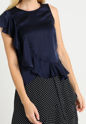 Top in satin blu Navy con spalla sinistra arricciata, abbinato a una gonna nera a pois. Tessuto morbido e elementi di design fluidi.
