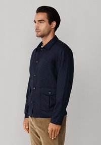 Marineblauwe, knoopjack in een gestructureerde stof met een puntige kraag, voorzakken en een rechte pasvorm. Draagt met beige corduroy broek.