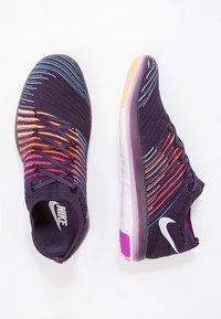 Nike urheilukengät, joissa on violetti neulosylä, värikkäitä vaaka-viivoja, valkoinen Swoosh-logo ja joustava pohja kontrastiväreissä.