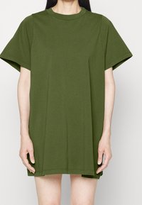 Oversized t-shirt klänning i olivgrön bomull. Korta ärmar, rund halsringning, rak skärning, sidokilar i fållen för ökad rörelsefrihet.