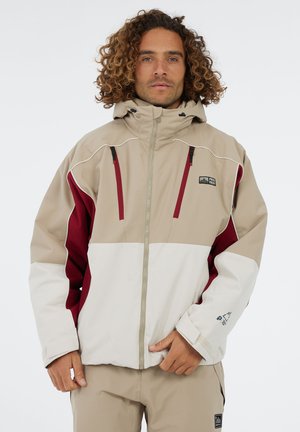 Beige, rode en witte waterdichte jas met een capuchon, rits aan de voorkant en contrasterende gekleurde panelen. Heeft zakken en logo-details.