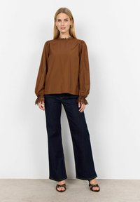 Brown long-sleeve blouse with lace trim at the collar and cuffs, paired with dark blue flared jeans and strappy open-toed sandals.