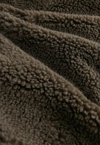 Bruine, gestructureerde stof met een donzige, zachte oppervlakte, met een gekreukt uiterlijk en een lichte glans, ideaal voor warme of comfortabele artikelen.