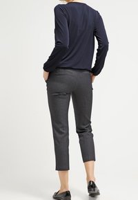 Marineblaues Langarmoberteil kombiniert mit grauen, cropped Hosen. Glattes Material mit subtiler Struktur. Flache Schuhe runden den Look ab.