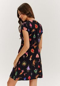 Čierne krátke šaty s farebnými, hravými potlačami srdiečok, slniečok a očí. Krátke rukávy a úzky pás pre priliehavý siluet.