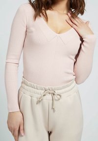 Haut à manches longues côtelé rose clair avec un col en V, assorti à un pantalon de jogging beige à cordon de serrage avec poches latérales et coupe décontractée.
