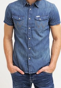 Kortärmad denimskjorta i mörkblått med två bröstfickor och W-sömmar, spetsig krage och knäppning.