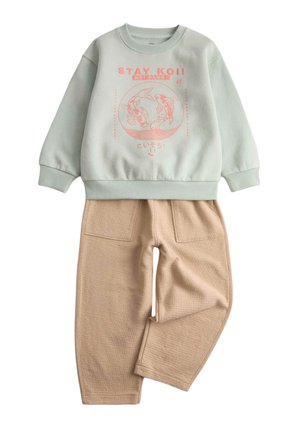 Felpa verde chiaro con grafica di pesci koi rosa e scritta "STAY KOI!" abbinata a pantaloni beige testurizzati con tasche frontali.
