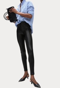 Modrý a bílý pruhovaný oversize svetr, vysoké černé kožené legíny a černé slingback podpatky. Modelka držící strukturovanou černou kabelku.