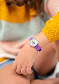 Montre en silicone violet avec un cadran rond, un cadran numéroté coloré et des accents argentés. Portée au poignet, mettant en valeur un design décontracté.