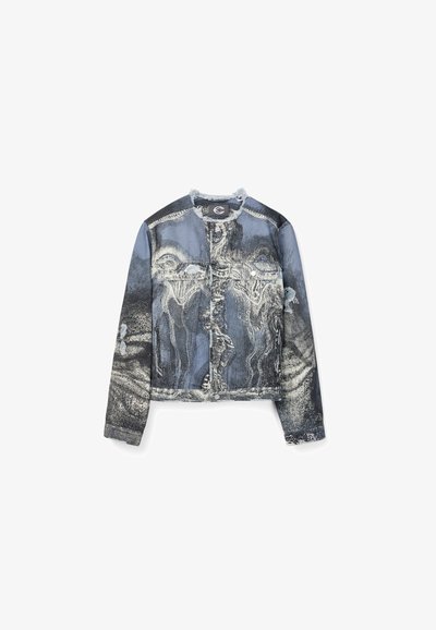 Veste en jean avec motifs blancs et noirs abstraits estompés, manches longues, boutons à l'avant et deux poches poitrine, présentée sur un fond blanc.