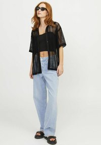 Maglietta nera a maniche corte in rete sopra un top corto nero, abbinata a jeans a gamba larga blu chiaro e sandali neri chunky.