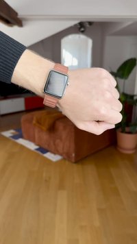 Έξυπνο ρολόι της Apple με τετράγωνη μεταλλική κάσα και ροζ-καφέ σιλικονούχο λουράκι. Το χέρι είναι ακίνητο πάνω σε ξύλινο δάπεδο.