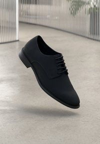Scarpa nera in pelle con lacci, finitura liscia, punta arrotondata e dettagli di cucitura discreti. Design leggero con suola in gomma a profilo basso.