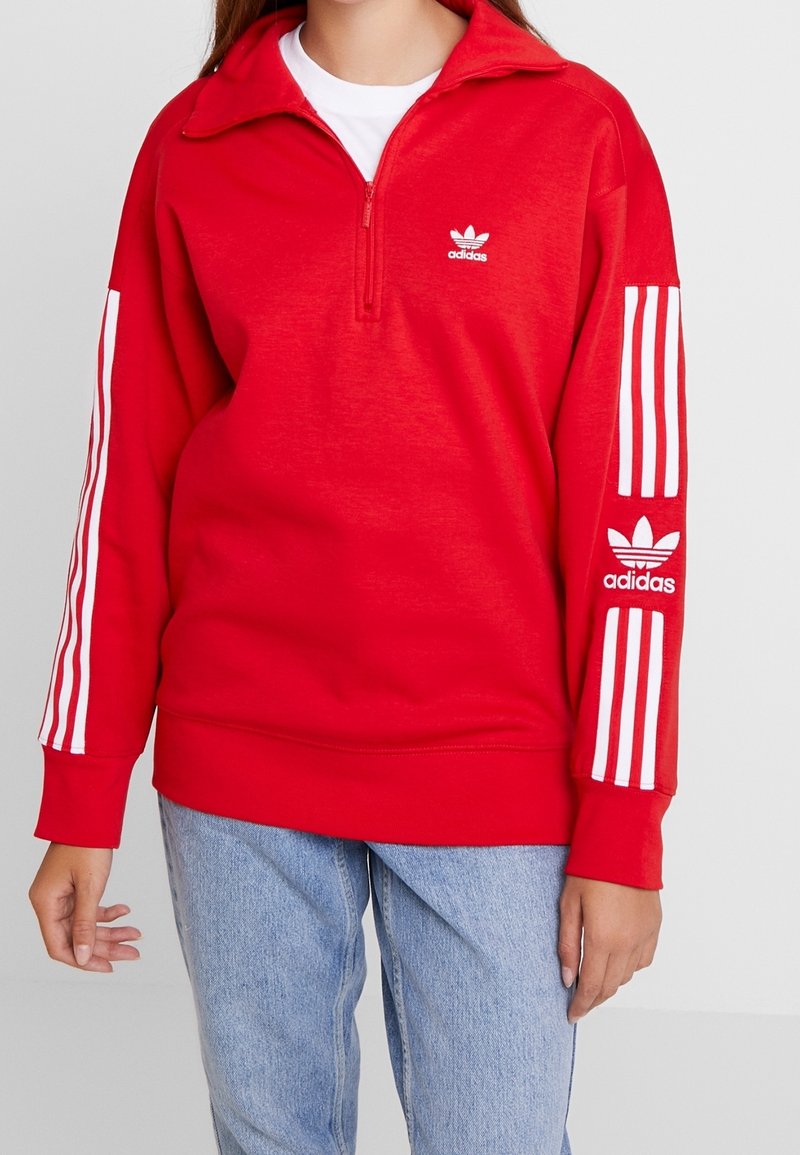 Červená mikina Adidas s čtvrtinovým zipem, bílým designem tří pruhů na rukávech a logem na hrudi. Měkký materiál z bavlněné směsi.