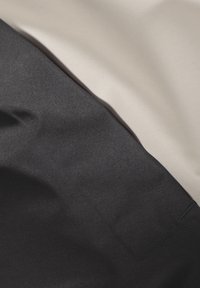 Due due campioni di tessuto sovrapposti: uno nero liscio, l'altro beige chiaro, entrambi con una leggera lucentezza e una superficie testurizzata.