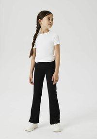 Biała koszulka z krótkim rękawem zestawiona z czarnymi dopasowanymi spodniami i białymi trampkami, o gładkiej fakturze i prostym, eleganckim wzornictwie.