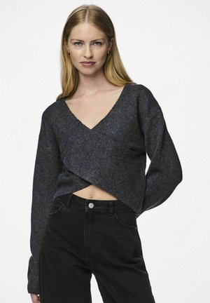 Maglione grigio scuro, corto, con scollatura a V e maniche lunghe, realizzato in un tessuto testurizzato. Indossato sopra jeans neri a vita alta.