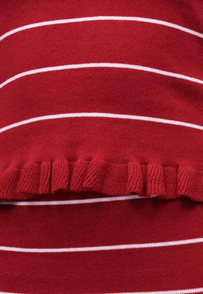 Κοντινή λήψη κόκκινου πλεκτού υφάσματος με οριζόντιες λευκές ρίγες και λεπτομέρεια με βολάν στην άκρη.