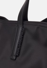 Schwarze Tragetasche aus Nylon mit einem gummierten "KARL LAGERFELD"-Etikett, robusten Griffen und nahtloser Verarbeitung. Glatte Textur und minimalistisches Design.