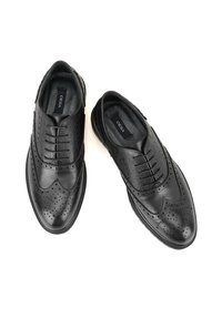 Zwarte leren schoenen met brogue-details, een gestructureerde bovenkant en een gladde neus. Voering met logo-label zichtbaar aan de binnenkant.