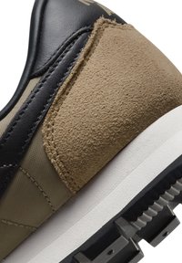 Nærbillede af sneakershæl, der har brun ruskind, olivengrønt stof, sorte læderdetaljer, hvid mellemsål og sort robust ydersål.