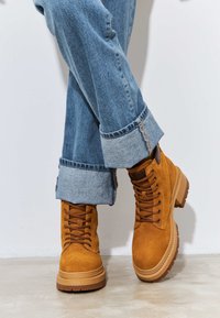 Bruine suède enkellaarzen met een gestructureerd oppervlak, ronde neus en rubberen zool. Combinatie met omgeslagen blauwe spijkerbroek.