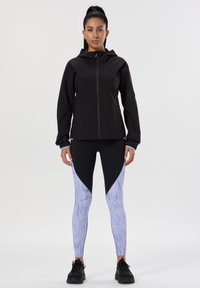 Giacca nera con zip frontale, abbinata a leggings marmorizzati neri e azzurri chiari. Design aderente con colori a contrasto e texture liscia.