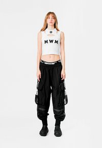 Top corto blanco con letras "MWM", combinado con pantalones cargo negros que cuentan con múltiples bolsillos y detalles de logotipo, llevados con calzado negro.