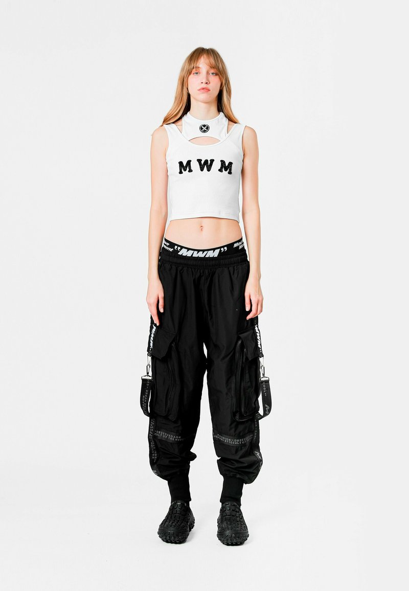 Top corto blanco con letras "MWM", combinado con pantalones cargo negros que cuentan con múltiples bolsillos y detalles de logotipo, llevados con calzado negro.