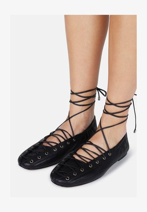 Juodos odos baleto bateliai su susikertančiomis raištelėmis ir metaliniais žiedeliais. Turi apvalų priekinį galą ir plokščią padą, pasižymi lygiu paviršiumi.