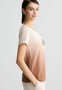 Short-sleeve, gradient t-shirt in cream and brown. Features a round neck and a textured print on the chest. Soft fabric with a relaxed fit.