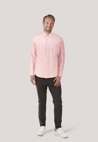 Hellrosa gestreifte Hemdbluse mit einer Tasche, kombiniert mit dunkler Hose und weißen Sneakern, zeigt ein lässiges Outfit-Design.