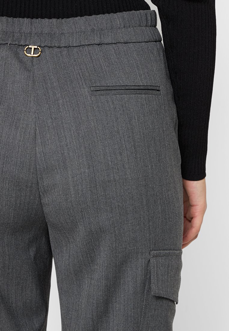 Graue maßgeschneiderte Hose mit strukturiertem Finish, featuring einen elastischen Bund, goldene Hardware-Akzente und eine seitliche Cargo-Tasche.