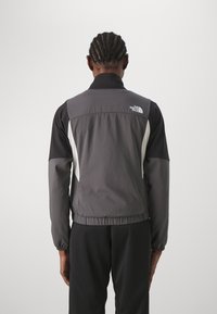 Giacca leggera e resistente all'acqua con una combinazione di colori nero e grigio, dotata di cerniera, elastico in vita e logo sul retro.