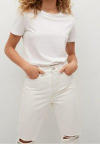 Bílý krátký rukáv tričko v kombinaci s vysokými, off-white džíny, které mají roztržené kolenní výřezy a klasický pětivreckový design.