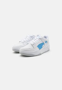 Baskets blanches en cuir, avec un accent bleu sur le côté, un bout texturé et des lacets plats, avec une semelle en caoutchouc épaisse.