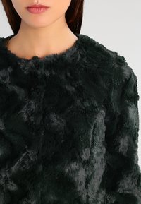 Grøn jakke i imiteret pels med en blød, tekstureret overflade. Kanter i rund halsudskæring og et fyldigt udseende, som fremhæver varme og komfort.