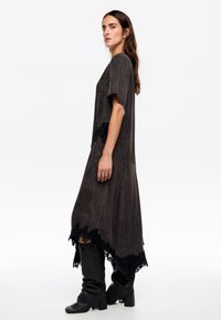 Vestido largo de color gris oscuro con un corte holgado, mangas cortas y un borde de encaje negro en el dobladillo. Textura suave y silueta asimétrica. Un par de botas negras hasta la rodilla.