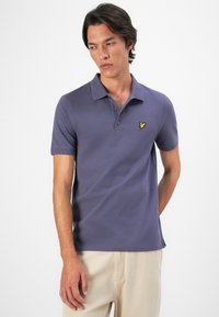 T-shirt polo violet en coton, doté d'un col classique, de trois boutons et d'un logo brodé jaune sur la poitrine gauche.